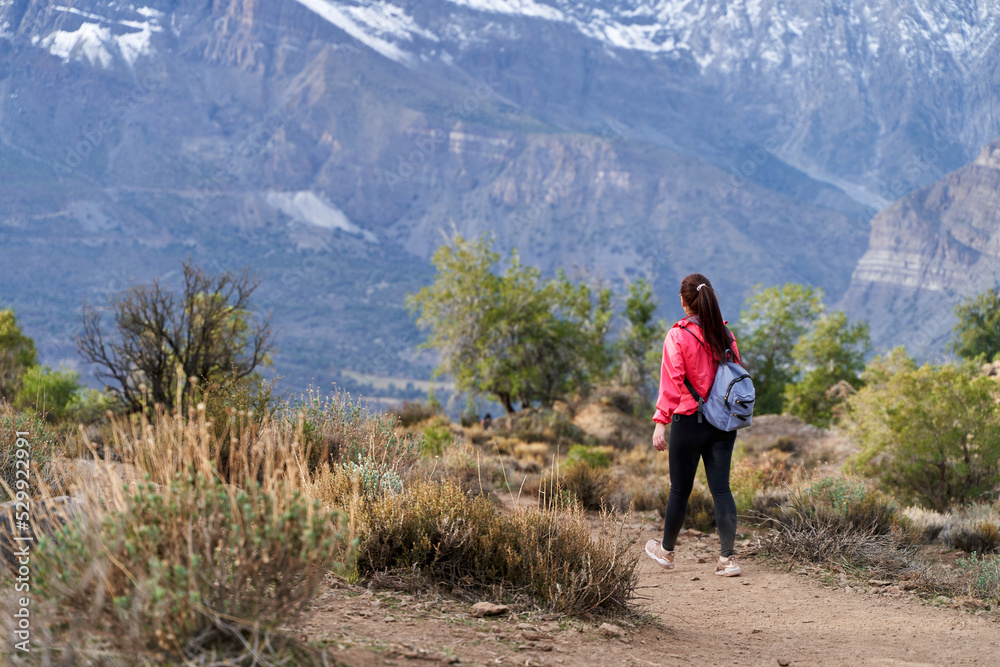 young woman with red jacket and backpack, descending the mountain in the middle of the Andes Mountains of Chile