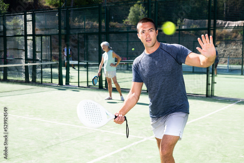 Male players playing padel in a padel court outdoor behind the net © JackF