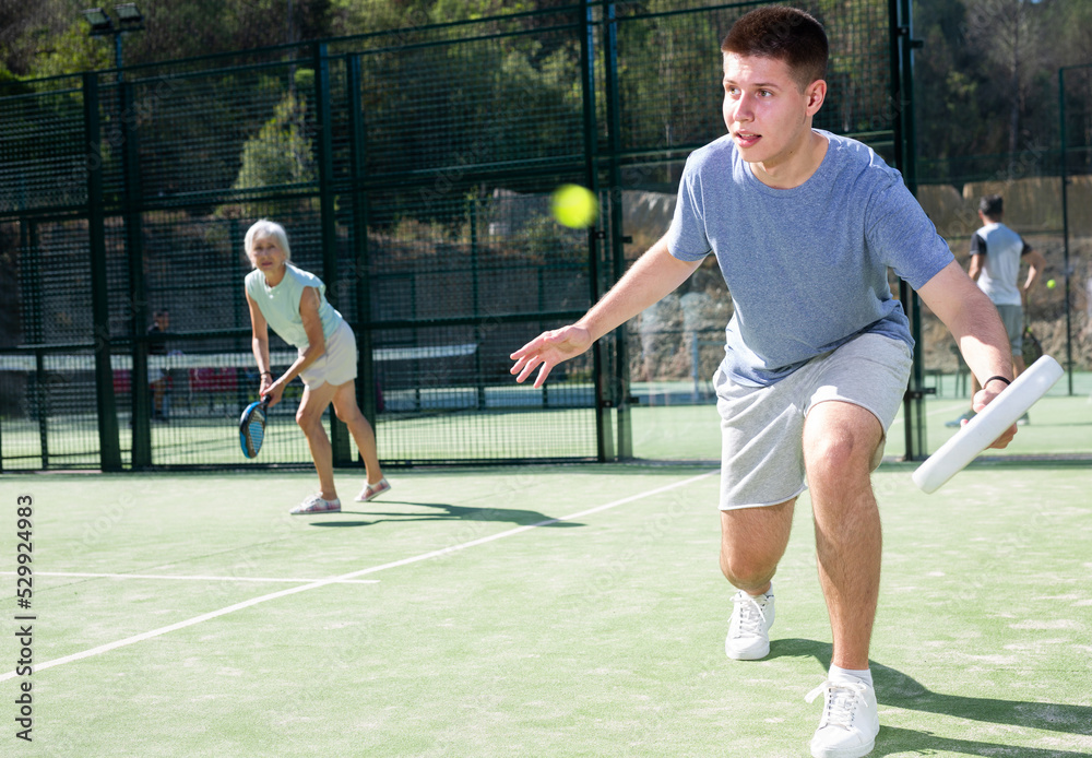 Young man in shorts and t-shirt playing padel tennis on court. Racket sport training outdoors.