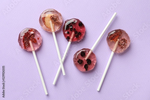 Sweet colorful lollipops with berries on lilac background, flat lay
