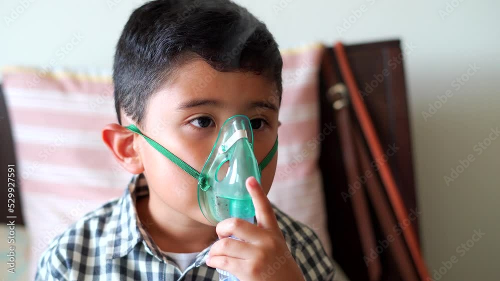 Sick child inhaling with nebulizer to reduce cough, lying at home