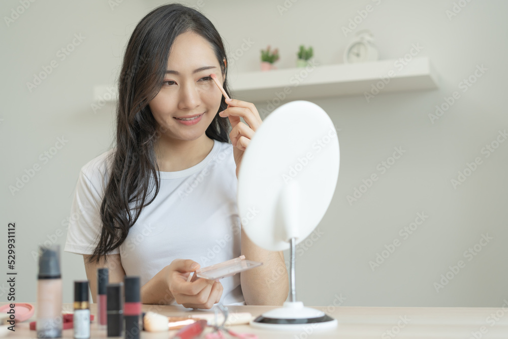 Daily makeup routine, Asian young women looks in the mirror during putting eyeshadow on her eyes.