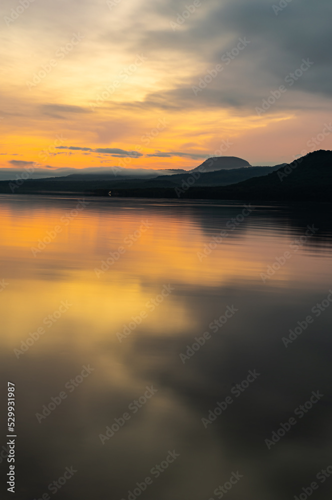 オレンジ色の夜明けの湖と山のシルエット。北海道の屈斜路湖。