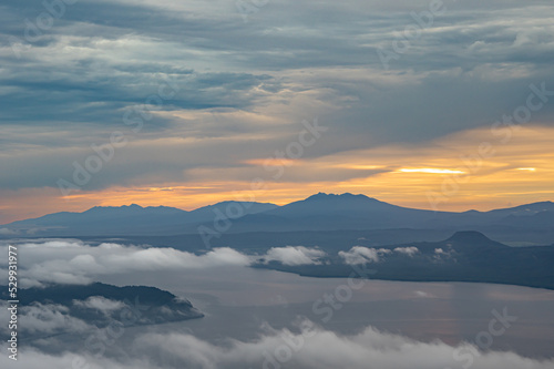 曇り空の朝の山のシルエットと湖の上に漂う雲。北海道の津別峠で。