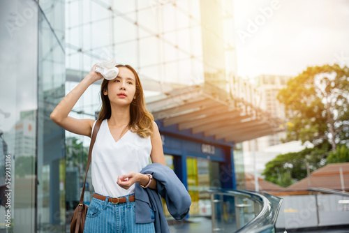 Angry female having sunstroke skin damage from sun UV city air pollution outside on street, Overheating Asian beautiful business woman drying sweat her face with cloth in warm summer day hot weather