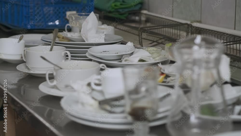 Dirty plates and glasses after a meal in the kitchen in the restaurant. Heap or pile of unclean glass and plates of breakfast or lunch table.