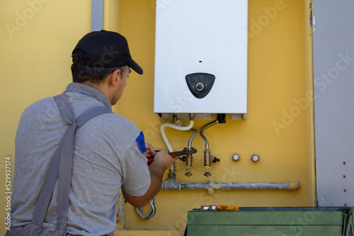 Plumber on a ladder with a wrench while repairing and servicing a gas boiler in anticipation of winter. Replacing a home central heating plumbing system
