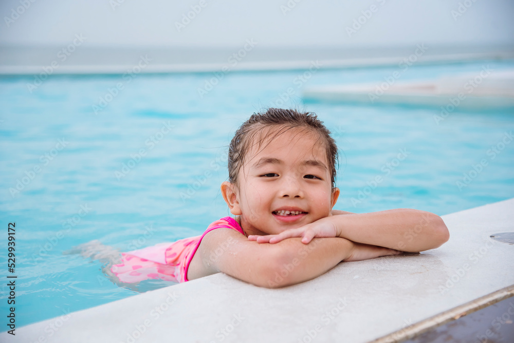 Toddler girl have fun swimming pool summer time with swimwear in blue water at hotel swimming pool outdoor. Kid swim playful water splash with happiness on summer vacation. Happy girl swim concept Toddler girl have fun swimming pool summer time with swimwear in blue water at hotel swimming pool outdoor. Kid swim playful water splash with happiness on summer vacation. Happy girl swim concept