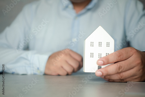 Man hands holding home model, small miniature white toy house. Mortgage property insurance dream moving home and real estate concept
