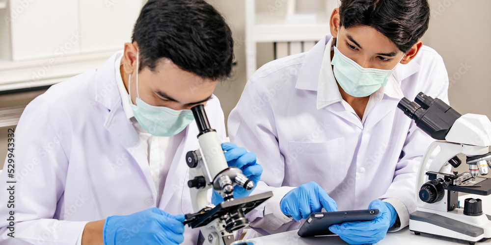 Two Male Scientists with Mask working in Lab while Checking Result of Blood Sample testing on Blue Tubes Foreground. Blue Tone. SARS-CoV-2 , Covid-19 THEME. Two Male Scientists with Mask working in Lab while Checking Result of Blood Sample testing on Blue Tubes Foreground. Blue Tone. SARS-CoV-2 , Covid-19 THEME.