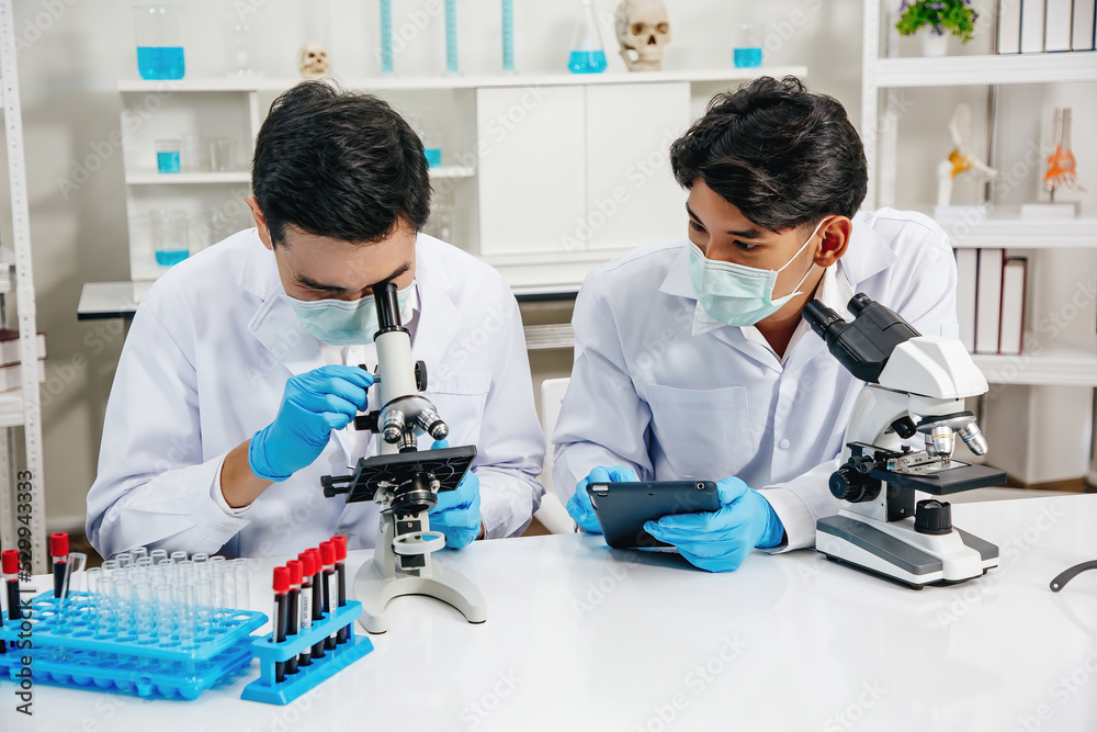 Two Male Scientists with Mask working in Lab while Checking Result of Blood Sample testing on Blue Tubes Foreground. Blue Tone. SARS-CoV-2 , Covid-19 THEME.