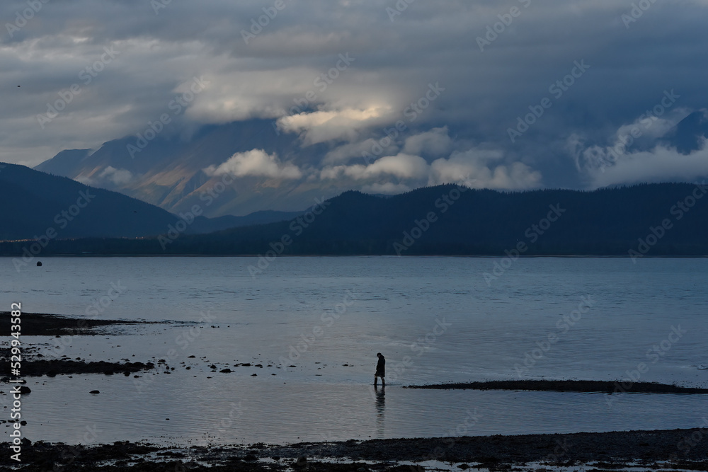 A man wades along the shore of Resurrection Bay near Seward, Alaska, at dusk.