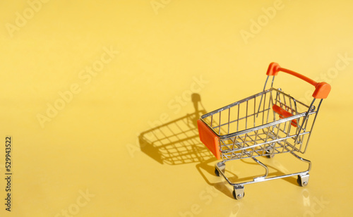 Small supermarket grocery push cart for shopping. Shopaholic. Buyer. Shopping concept. Close-up. Isolated shopping trolley on a yellow background. Copy space.