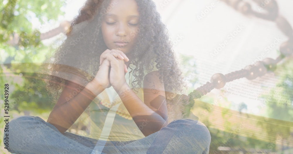 Naklejka premium Multiple exposure of biracial elementary girl praying against trees and rosary on bible