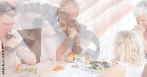 Multiple exposure of caucasain family praying at dinning table and hand with rosary in background photo