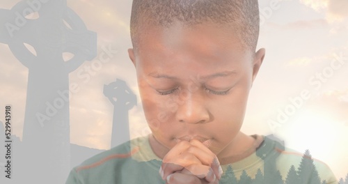 Multiple exposure of african american elementary boy praying with cemetery crosses against sky