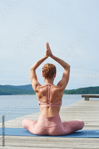 back view mature woman in pink sportswear practices yoga on a wooden deck near the sea.