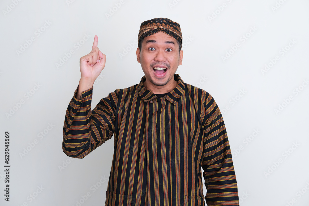 Asian man wearing traditional Javanese costume pointing up with excited expression Asian man wearing traditional Javanese costume pointing up with excited expression