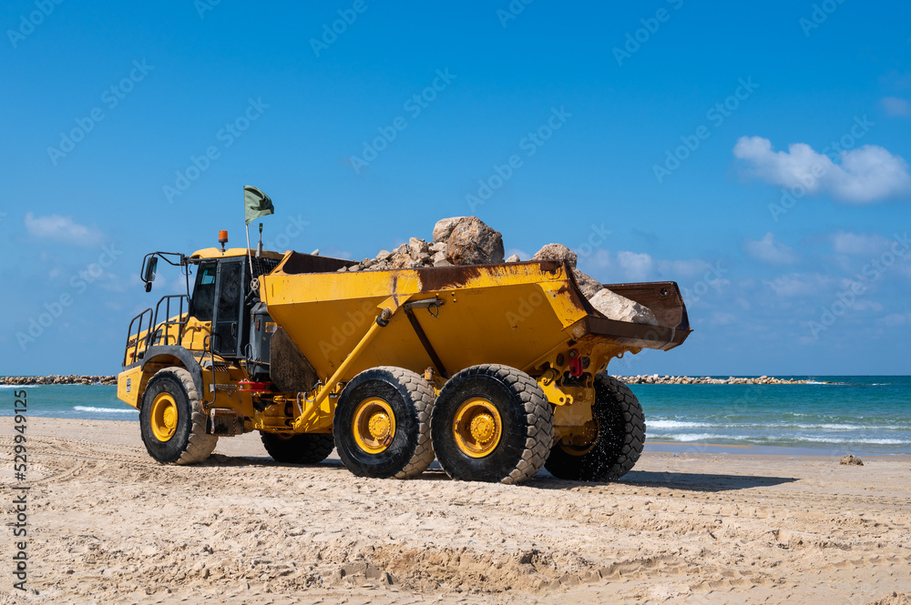 A large mining truck transports stones to build breakwaters to protect a beach in Netanya, Israel. A large mining truck transports stones to build breakwaters to protect a beach in Netanya, Israel.