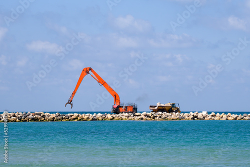 An excavator and a mining truck move stones into the sea. Construction of breakwaters to protect the beach in Netanya in Israel. © Uri