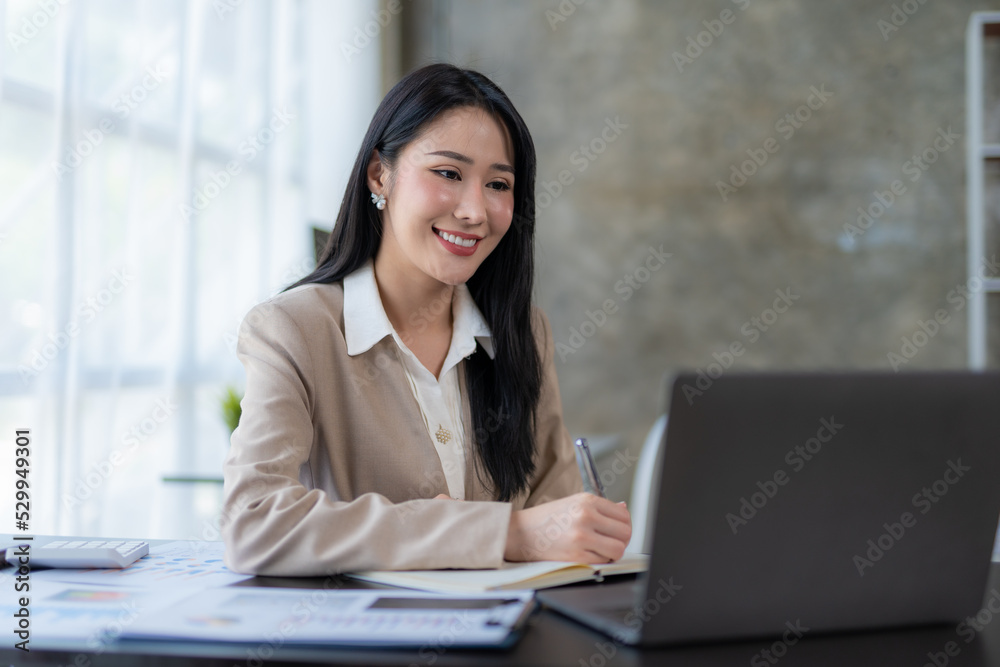 Beautiful Asian business woman using her laptop to work and enjoy working, taking note, reviewing assignment and smiling in the office. Beautiful Asian business woman using her laptop to work and enjoy working, taking note, reviewing assignment and smiling in the office.