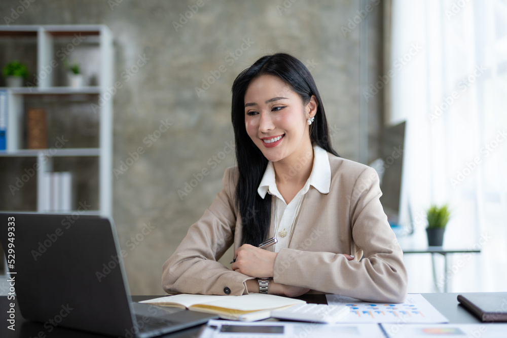 Beautiful Asian business woman using her laptop to work and enjoy working, taking note, reviewing assignment and smiling in the office. Beautiful Asian business woman using her laptop to work and enjoy working, taking note, reviewing assignment and smiling in the office.