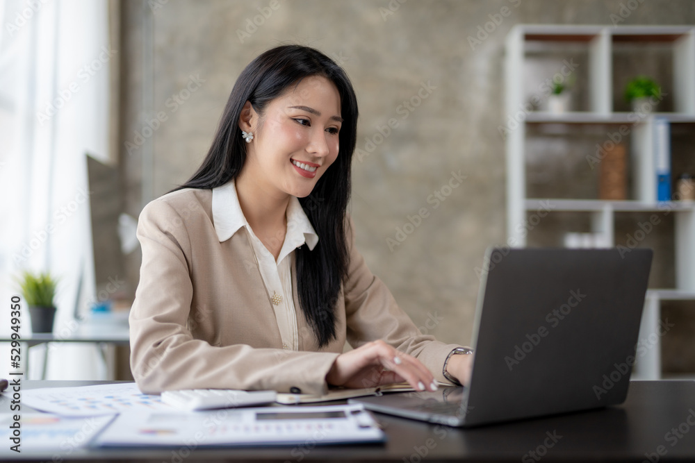 Beautiful Asian business woman using her laptop to work and enjoy working, taking note, reviewing assignment and smiling in the office. Beautiful Asian business woman using her laptop to work and enjoy working, taking note, reviewing assignment and smiling in the office.