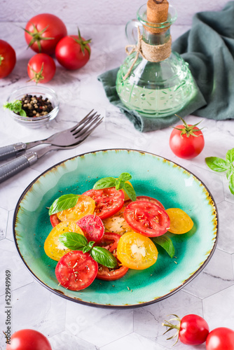 Fresh salad of yellow and red tomatoes with basil leaves on a plate on the table. Vertical view