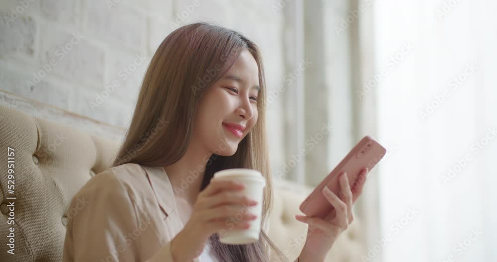 Beautiful smiling asian woman sitting at coffee shop using smartphone texting sharing messages on social media. Attractive satisfied female holding phone enjoying mobile technology. Relax and calm. Beautiful smiling asian woman sitting at coffee shop using smartphone texting sharing messages on social media. Attractive satisfied female holding phone enjoying mobile technology. Relax and calm.