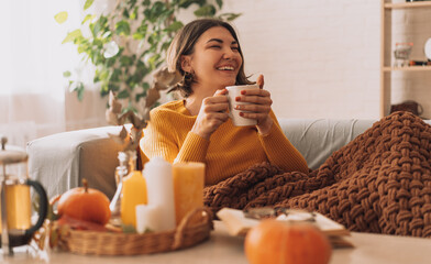 Lady drinks herbal tea brewed in a teapot in front of burning candles and a pumpkin/