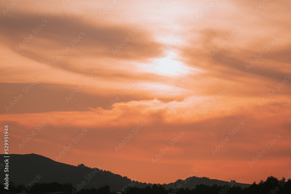 Red sunset, sun behind clouds and mountains.