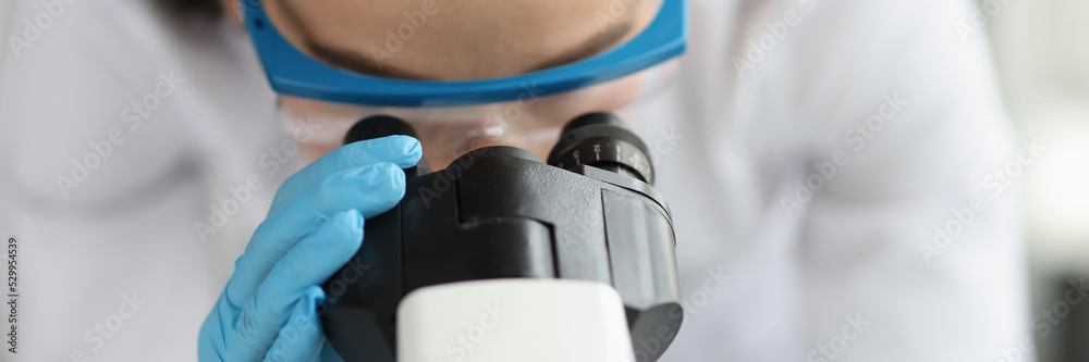 Woman doctor scientist looking through microscope in clinic