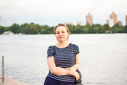 A girl in a striped jacket is standing on the river embankment, leaning on the parapet, looking into the distance. Evening walk around the city.