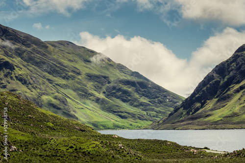 Mountains of Connemara, beautiful nature scene in Ireland with green tall mountains in low clouds and lake. Warm sunny day. Travel and sightseeing. Irish landscape and nature.