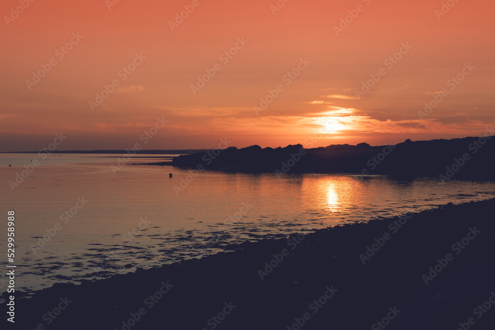 Obraz premium Sunset nature scene by the ocean. Silhouette of the ocean coast. Warm orange color.