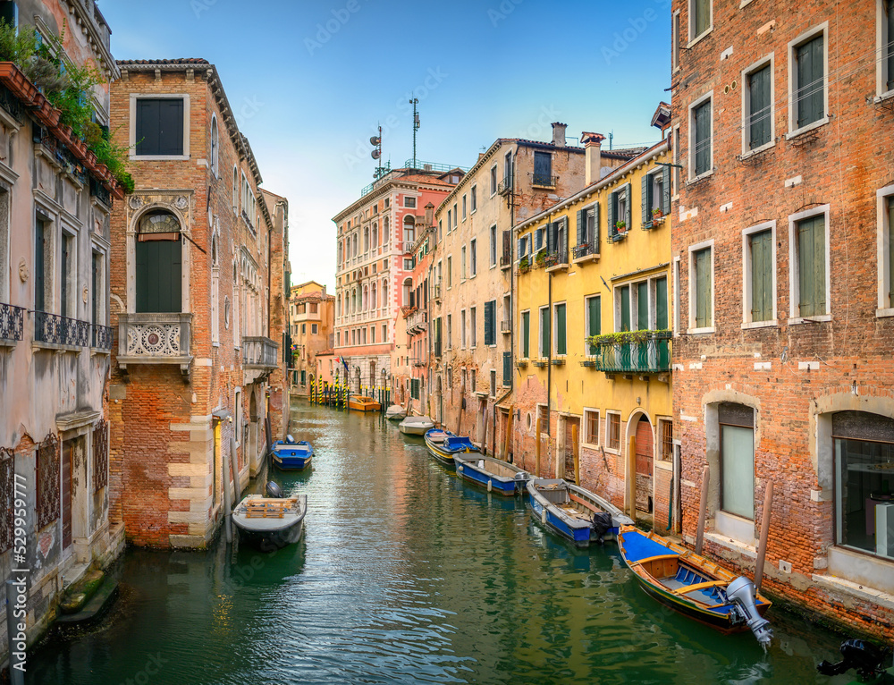View on the narrow cozy streets of the canals with parked boats in Venice, Italy. Architecture and landmark of Venice.