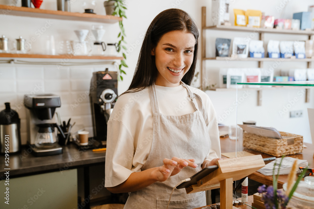 White barista woman wearing apron working with tablet computer in cafe