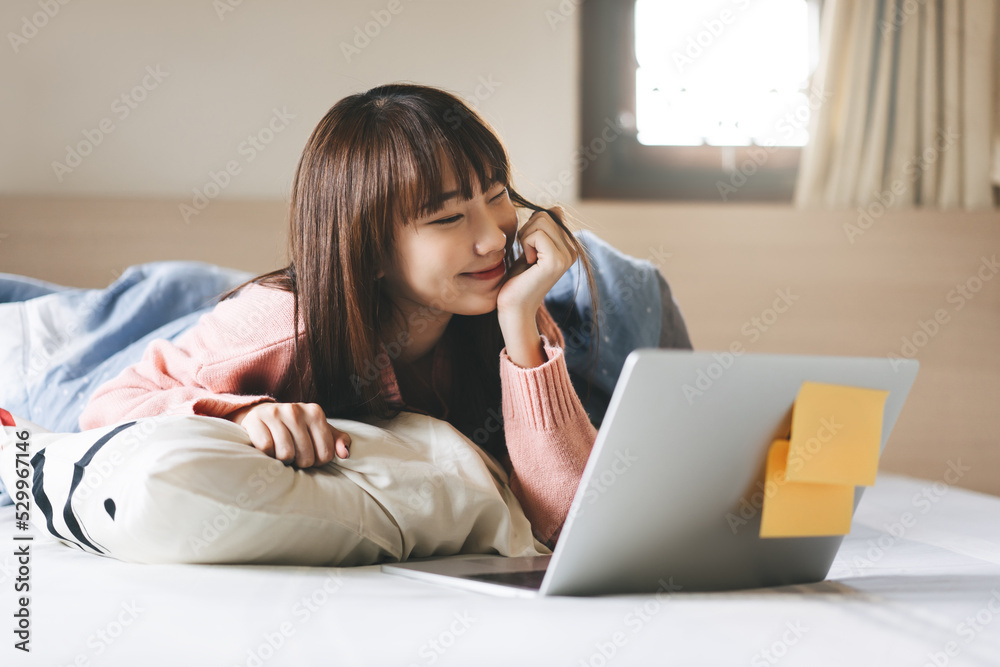 Relax cute young adult single woman using laptop at bedroom on morning time for shopping or dating online Relax cute young adult single woman using laptop at bedroom on morning time for shopping or dating online