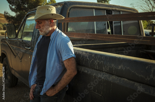 Portrait of adult man in cowboy hat standing against a vintage truck during sunset