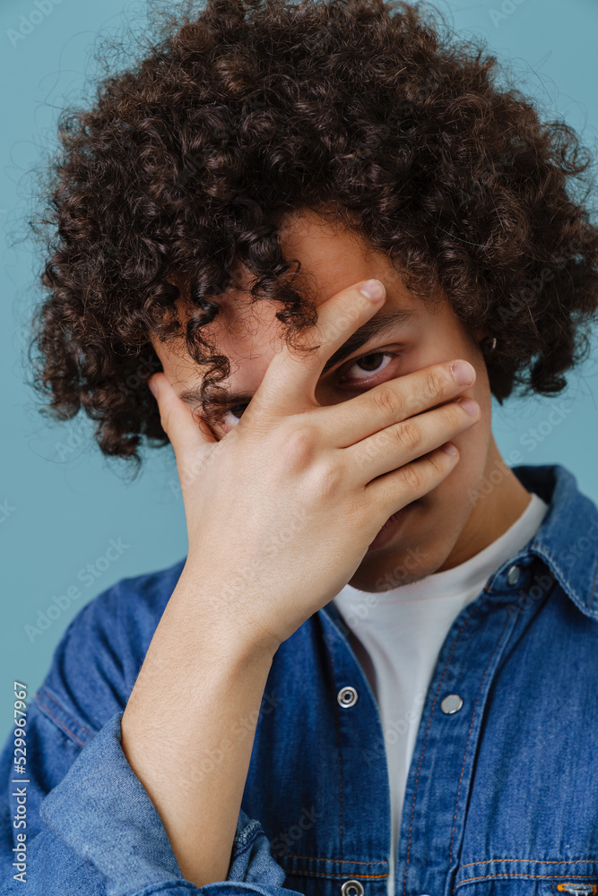 Curly young man wearing denim shirt covering his face Curly young man wearing denim shirt covering his face