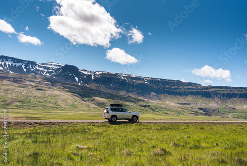 Large car parked on dirt road among the mountain and meadow on sunny day in summer