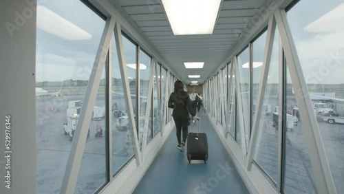 Slow motion footage of a person with a roller bag suitcase walking down the jetway towards a plane. photo