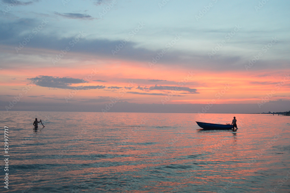 Fototapeta premium Silhouette of a boat near the shore against the background of the setting orange sun