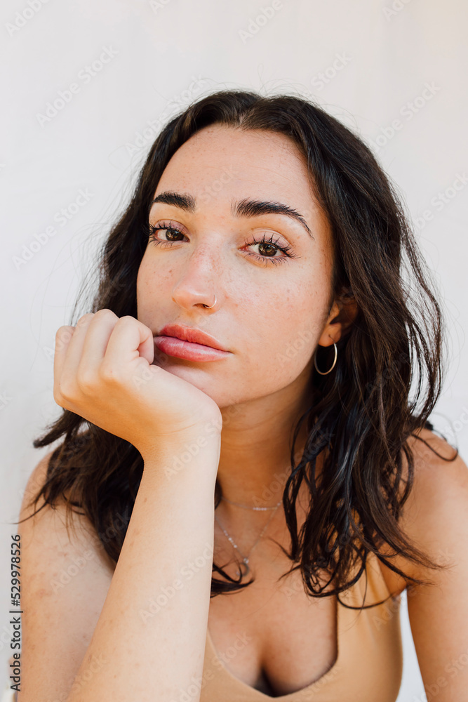 Beautiful young woman with hand on chin in front of white wall Beautiful young woman with hand on chin in front of white wall