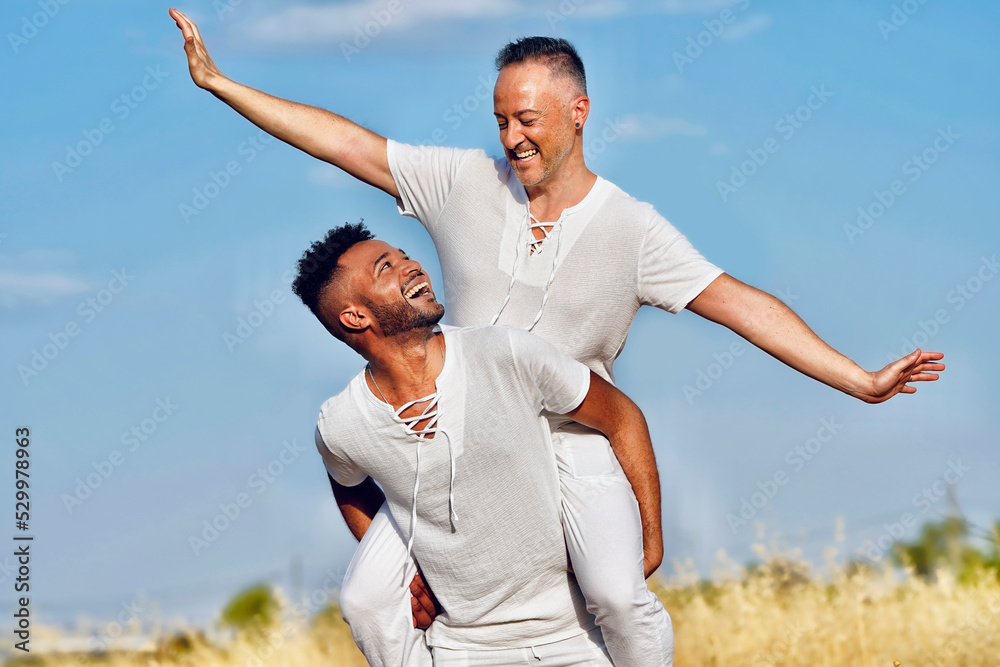 Young man piggybacking boyfriend on sunny day Young man piggybacking boyfriend on sunny day