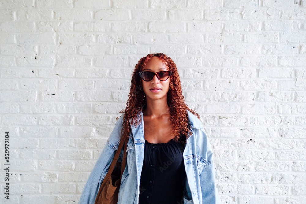 Smiling young woman wearing sunglasses standing in front of wall Smiling young woman wearing sunglasses standing in front of wall