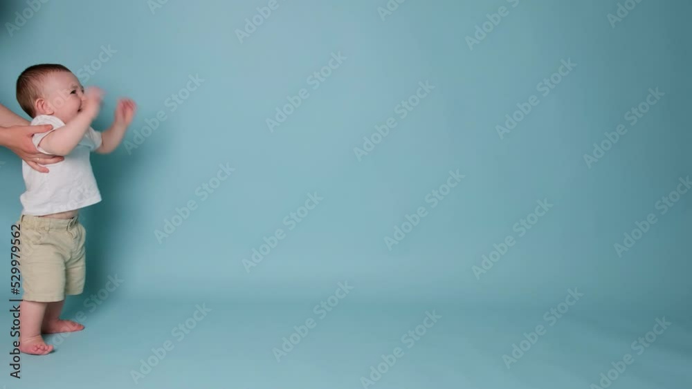 Happy toddler baby learns to walk and takes his first steps. Child boy walks for the first time on a studio blue background. Kid age one year, slow motion