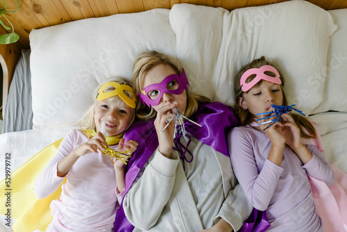 Mother and daughters with party horn blower lying on bed at home photo