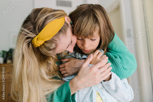 Mother embracing depressed daughter from behind at home photo