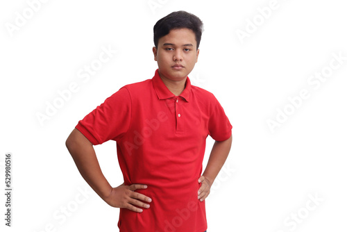 Serious Asian man in red polo shirt with confident or displeased expression, keeps both hands on hips, isolated on white background. Guy looking at camera with anger. Emotions and signs concept